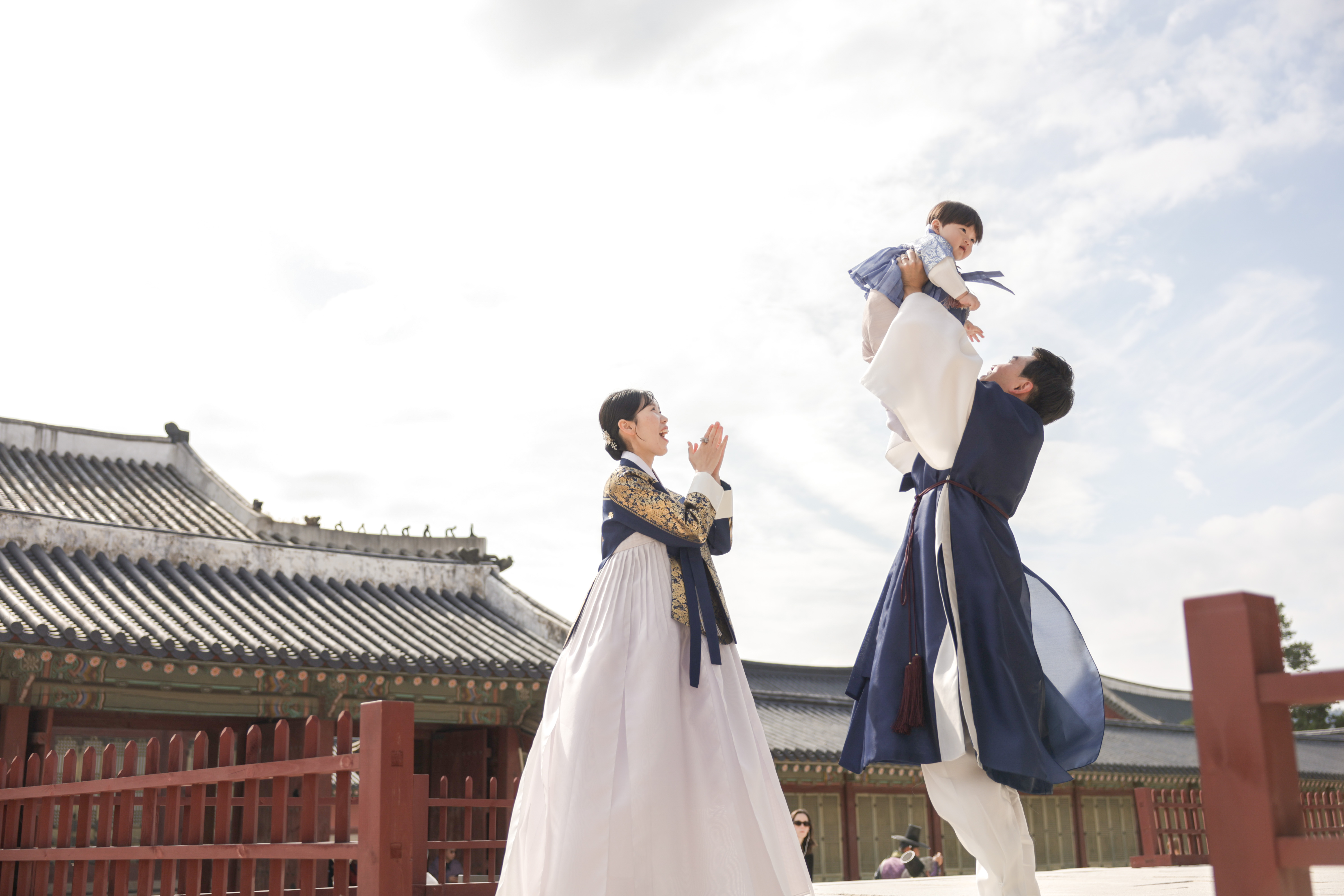 한옥 앞에서 아기를 들어 올리고 있는 부모님